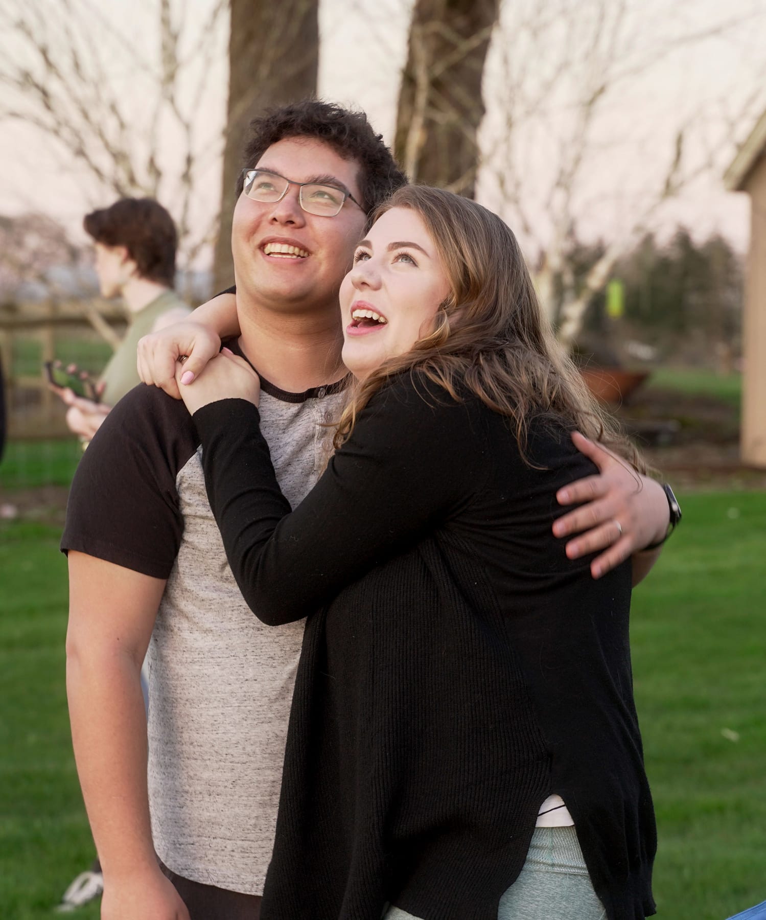 An engaged couple hugs and laughs in warm evening light.