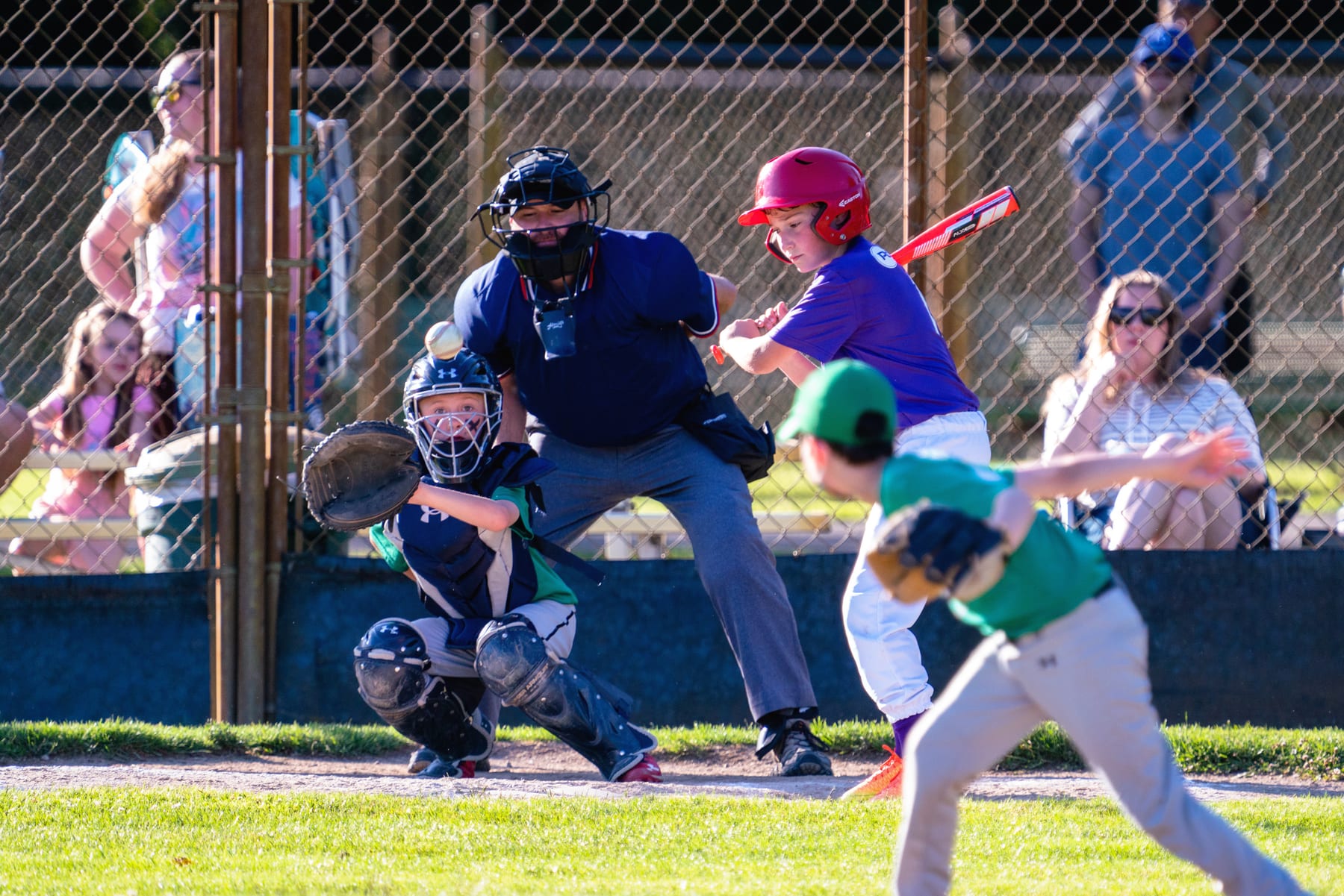 A young batter swings as family cheers behind the backstop.