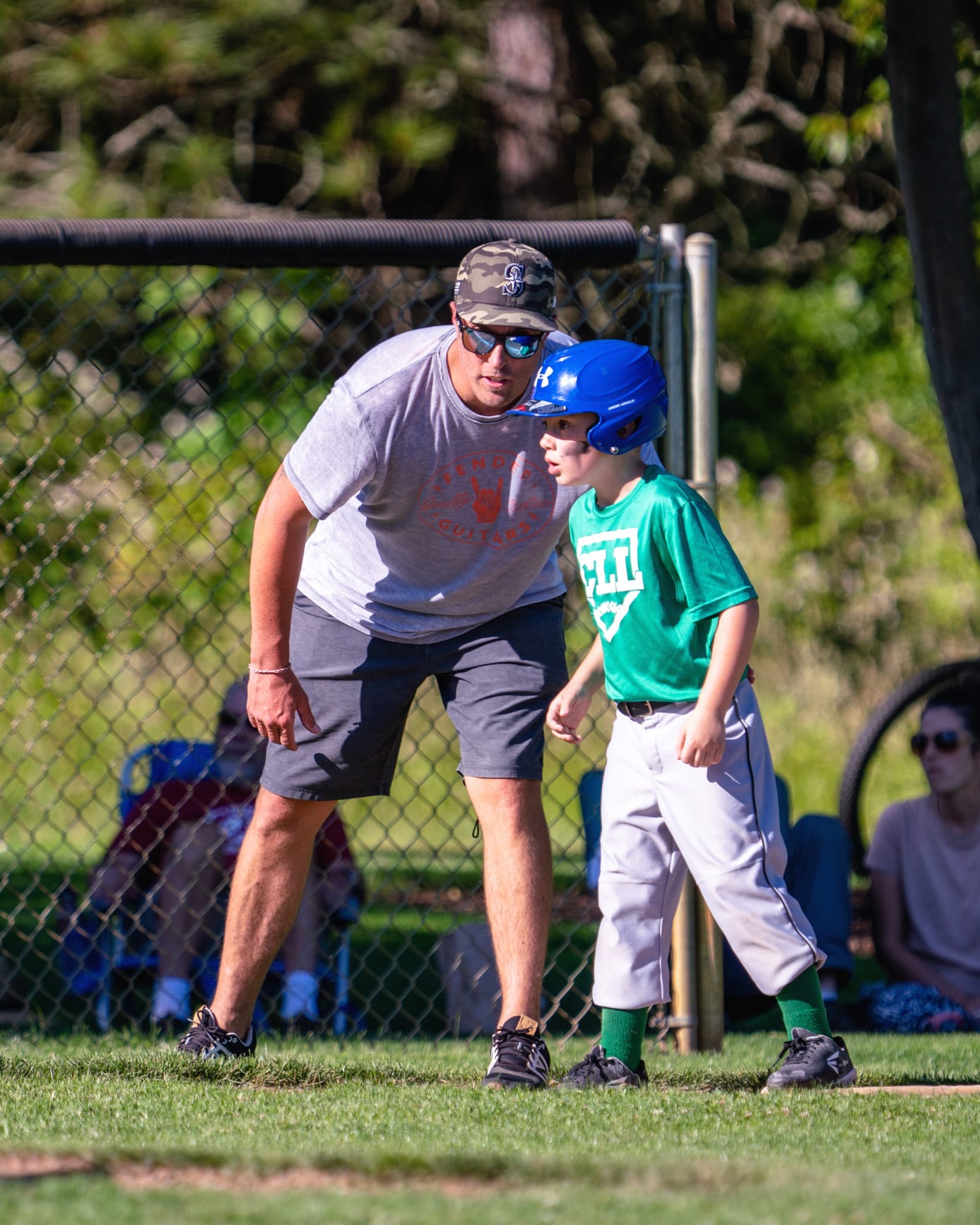 A father crouches beside his young son at a baseball field.