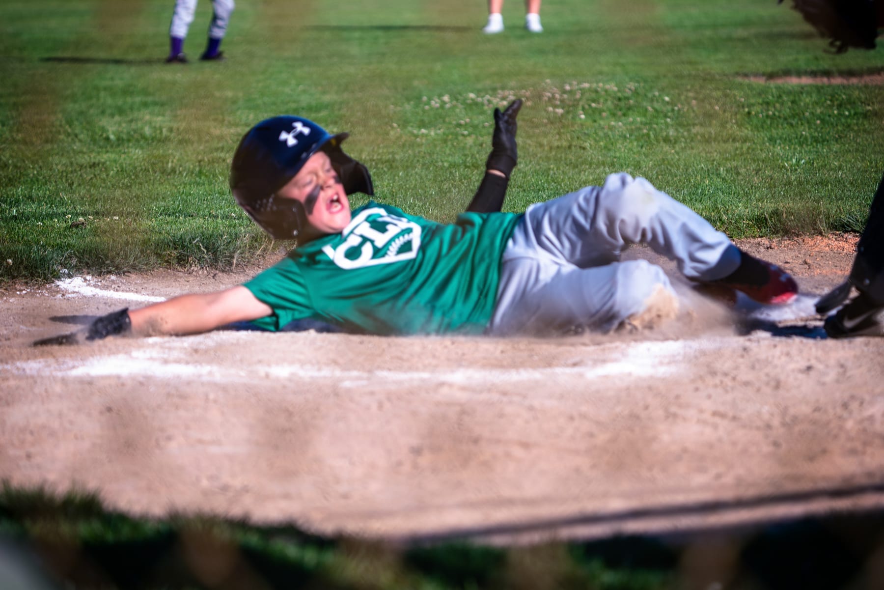 A boy slides into home plate with his arms in the air.