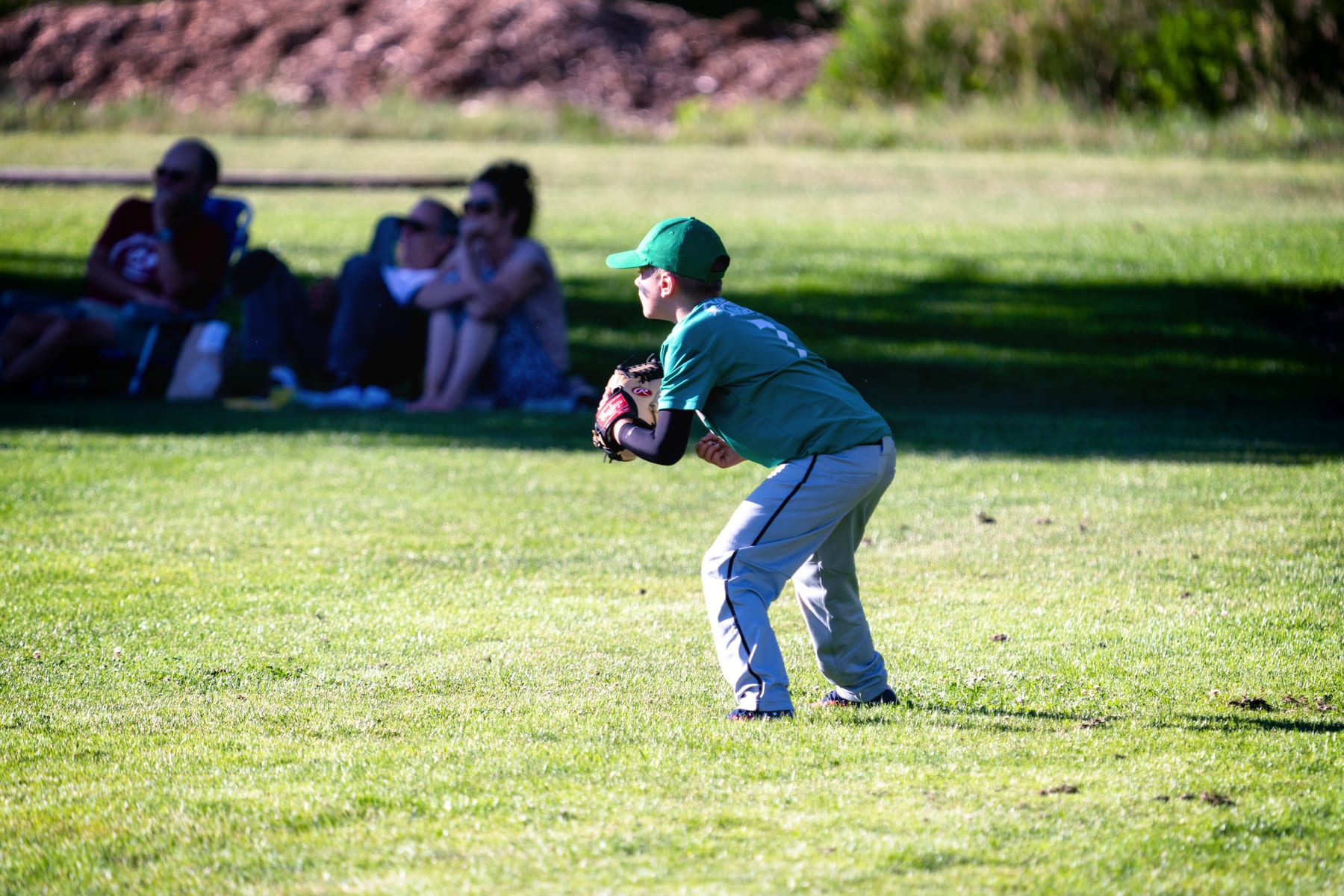 A boy in a green cap plays catch while his family watches from the grass.