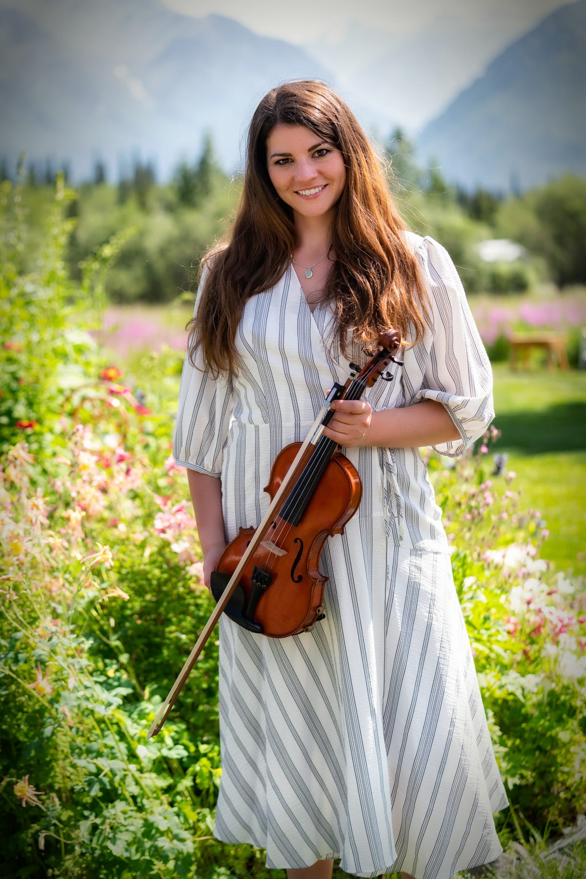 A senior holds her violin among wildflowers in a mountain valley.