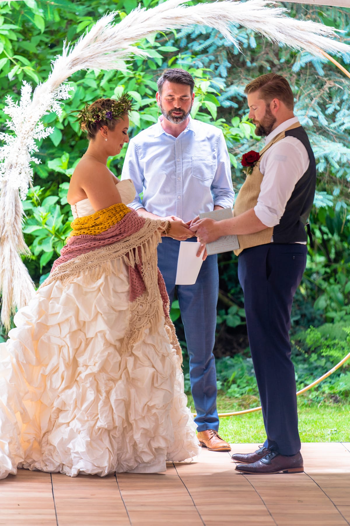 A couple exchanges vows beneath a pampas grass arch in a backyard ceremony.