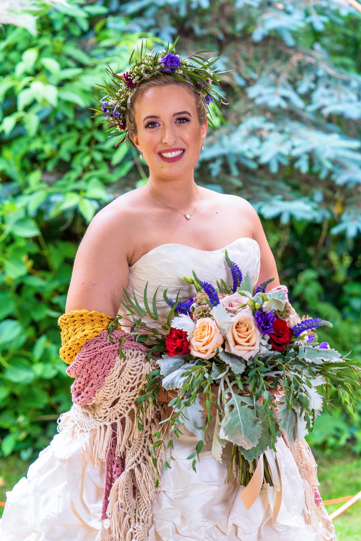 A bride in a floral crown holds her bouquet in a garden.