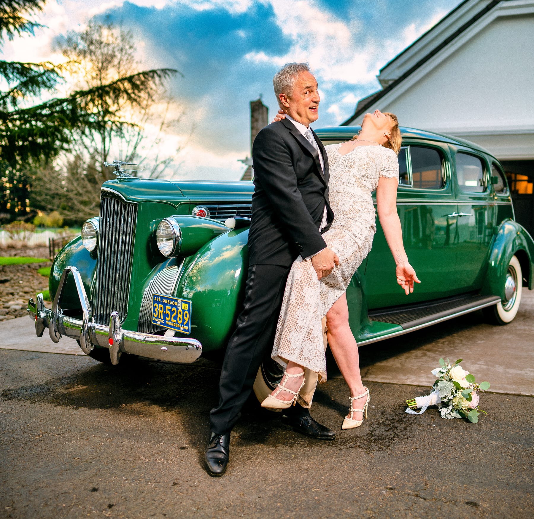 A couple laughs together beside a vintage green Packard.
