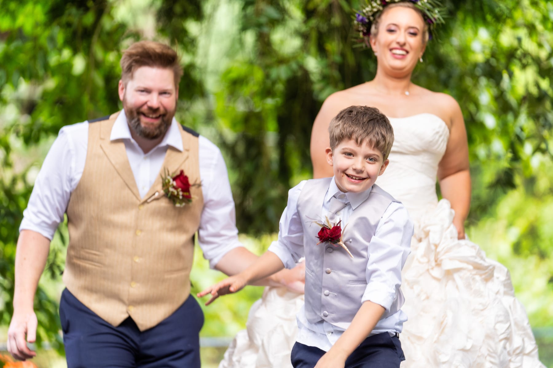 A couple runs across the lawn with their son on their wedding day.