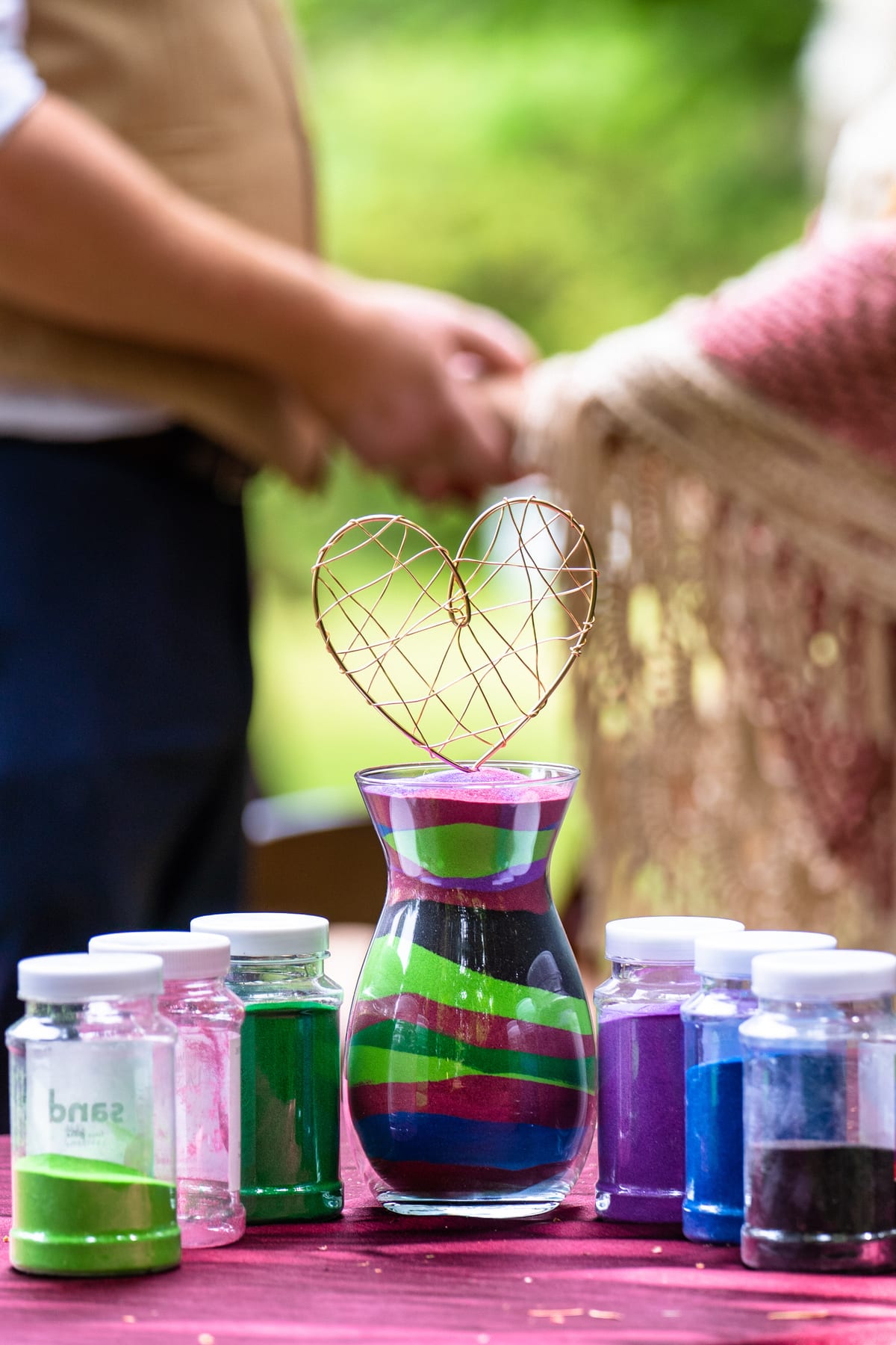 Hands pour colored sand together during a unity ceremony.