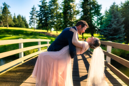A newlywed couple sharing a kiss on a bridge.